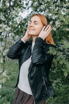 A red-haired teenage girl listens to music in headphones, configured via the phone. The time of spring flowering of cherry orchards.