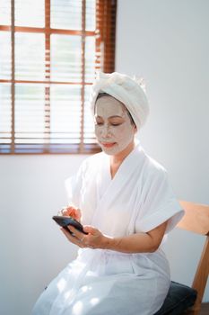 Portrait of elderly woman doing face spa treatment and using mobile phone