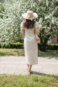 An attractive long-haired woman walks in the spring in the park of blooming apple trees. Spring portrait of a woman