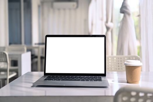 Computer laptop and coffee cup on white table in modern cafe.