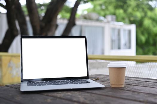 Mock up computer laptop and coffee cup on wooden table at outdoor.