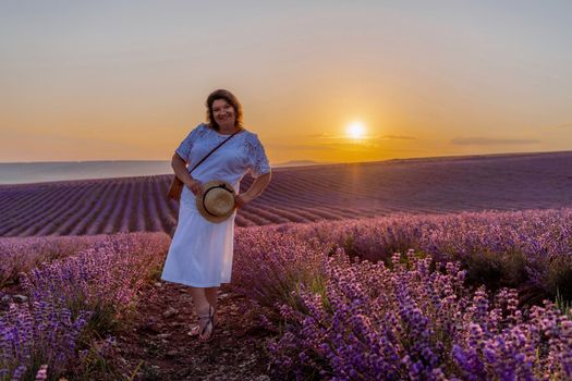 Woman lavender field sunset. Romantic woman walks through the lavender fields. illuminated by sunset sunlight. She wears a white blouse and a white skirt with a hat