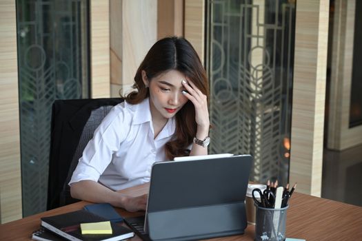 Stressed businesswoman holding her head while checking information on computer tablet.