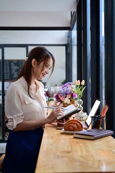 Side view smiling young woman sitting near window in cafe and using laptop computer.