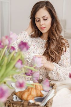 A brown-haired woman with long hair is having breakfast at the table with croissants and a cup of coffee. Spring portrait