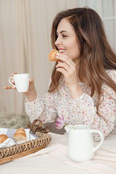 A brown-haired woman with long hair is having breakfast at the table with croissants and a cup of coffee. Spring portrait