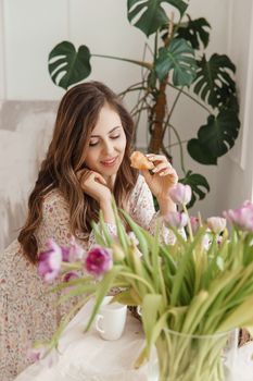 A brown-haired woman with long hair is having breakfast at the table with croissants and a cup of coffee. Spring portrait