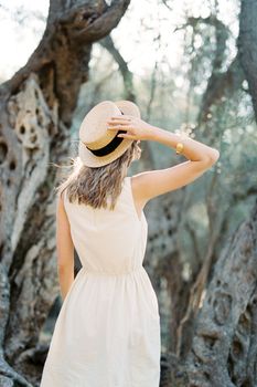 Girl stands in front of a tree holding a straw hat with her hand. Back view. High quality photo