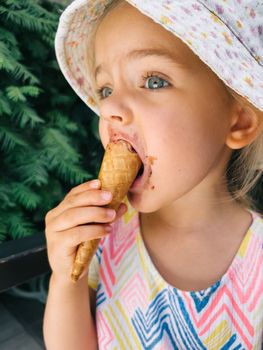 Little girl eating ice cream in a waffle cone holding it with her hand. High quality photo