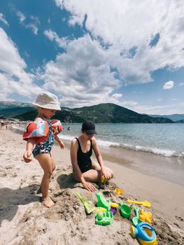 Little girl in inflatable armlets stands on the beach next to her mother. High quality photo