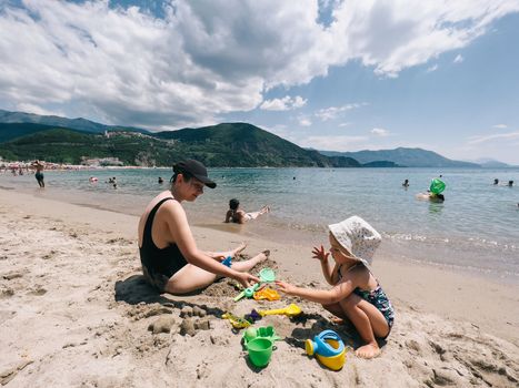 Mom with a little girl sculpt sand figures with plastic molds on the seashore. High quality photo