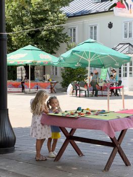 Little girls stand on the street near the table with felt-tip pens and look at it. High quality photo