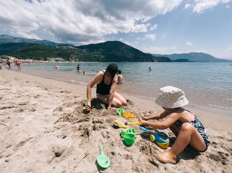 Mom and little girl are sitting on the beach and sculpting sand figures. High quality photo