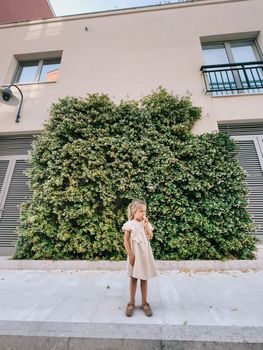 Little girl eating ice cream cone near the green hedge near the house. High quality photo