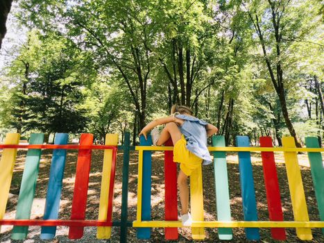 Little girl climbs over a colored fence in the playground. High quality photo