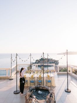 Photographer girl photographing a set table on the terrace of a restaurant overlooking the island of Sveti Stefan. High quality photo