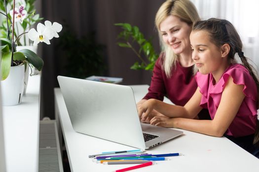 Happy teacher and student girl sitting at working desk in classroom. Cheerful young mother and child sitting at table and smiling. Little kid and her private language tutor.