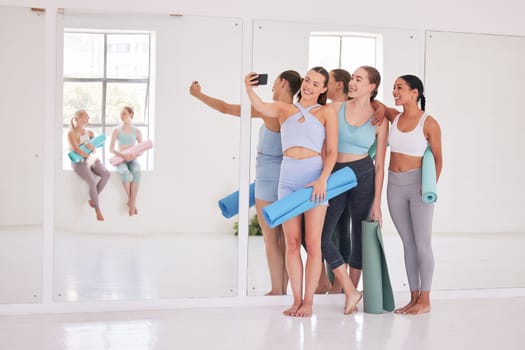 Group of friends taking a selfie in yoga studio. Young women using cellphone before yoga class. Group of happy women bonding before a workout. Young friends taking a photo in yoga class.