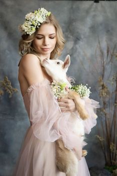 A young blonde woman in an airy pink dress with a white kid. Spring portrait of a woman