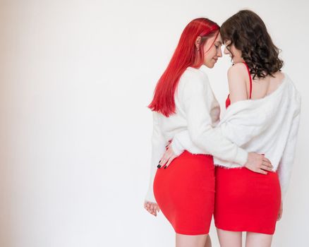 Rear view of two women dressed in identical red dresses and white sweaters. Lesbian intimacy. White background