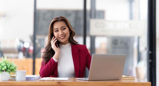 Smiling beautiful Asian businesswoman analyzing chart and graph showing changes on the market and holding smartphone at office.