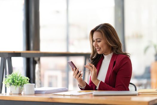 Happy businesswoman using mobile phone while working at office with laptop.