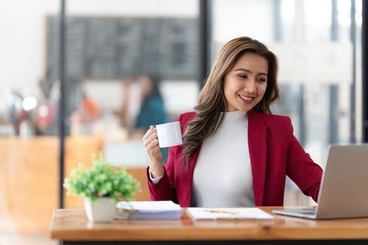 Young Asian businesswoman working and holding hot coffee cup in the office room.