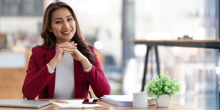 Young businesswoman working at her laptop and going over paperwork while sitting at a desk in an office.