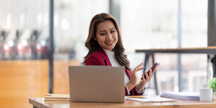 Happy businesswoman using mobile phone while working at office with laptop.