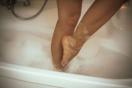 Women's feet in bath foam. View from above. Enjoy and relax in a spa hotel.