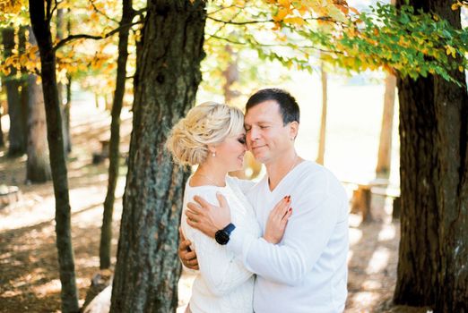Man and woman hugging, leaning their heads against each other, standing near a tree. High quality photo