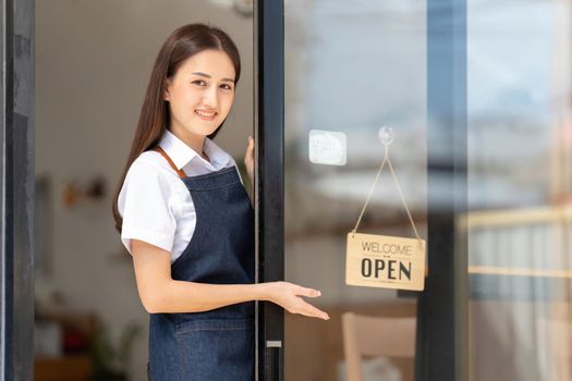 Happy waitress standing at restaurant entrance. Mature business womanattend new customers in her coffee shop. Happy woman owner showing open sign in her small business shop.