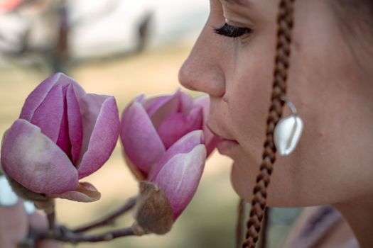 Magnolia flowers, a girl smells a blooming magnolia in the park in the sun, enjoys her vacation