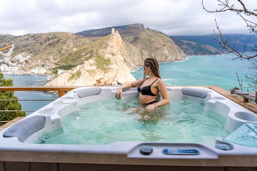 Take time for yourself. Outdoor swimsuit with mountain and sea views. A woman in a black swimsuit is relaxing in the hotel pool, admiring the view.