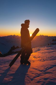 A skier stands on top of a snowy hill at a ski resort during a calm winter sunset. Athlete scenery, wallpaper with place for your montage.