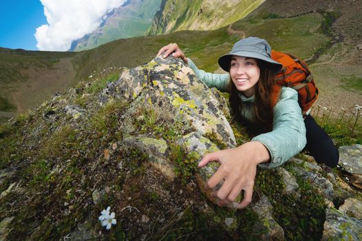 a young tourist woman smiles and climbs to the top of the cliff with a backpack. climbing a steep slope in a deep mountain canyon during hiking and climbing.