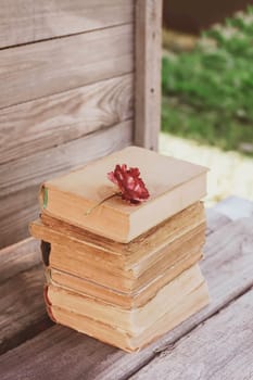 Vintage card with stack of old books and red rose flower outdoors