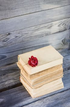 Vintage card with stack of old books and red rose flower outdoors