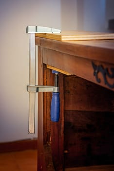 Restoration of an antique French wooden furniture using wood clamps to attach different parts of it