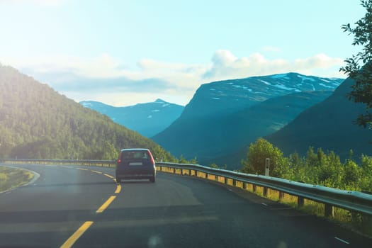 journey to the north, a small car rides against the backdrop of snow-capped mountains , summer evening