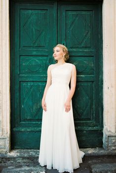 Bride in a white dress stands leaning against a green door. High quality photo