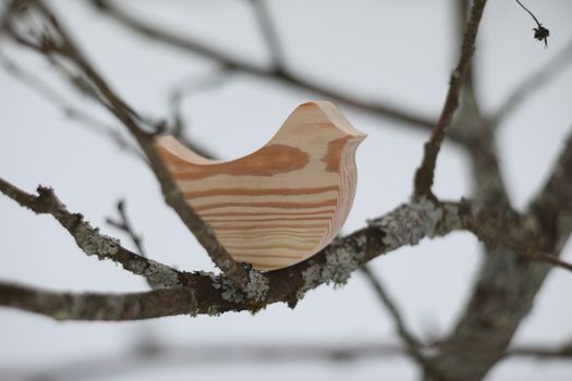 Wooden handmade toy bird on the tree branch on a winter day. Hello Spring concept. Winter landscape