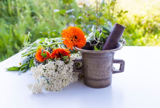 The brass mortar and the bouquet of Calendula and Yarrow medical plants on the table outdoors.