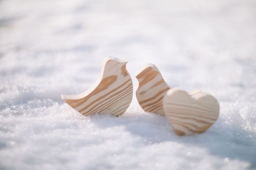 Beautiful decorative small wooden toy birds on white snow in winter. Easter, Spring decoration. Handmade wooden toys.