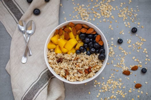 Oatmeal porridge with blueberries, mango and almonds in bowl on concrete grey table from above. flatlay. Healthy breakfast food. Copy space