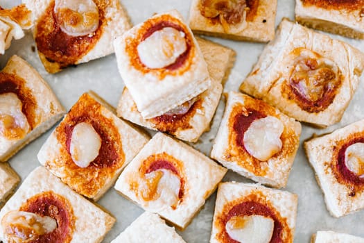 Mini pizzas with mozzarella cheese and fresh basil on a on white baking paper, close-up, top view.