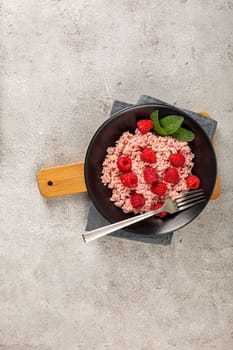 Healthy food on gray concrete background. Fresh raspberries risotto on a delicate and elegant dish. Vertical orientation. Space for text.