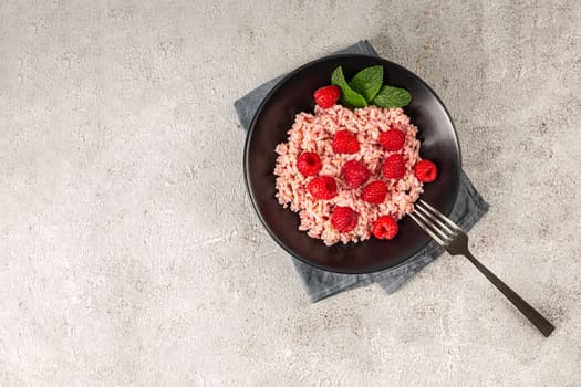 Healthy food on gray concrete background. Fresh raspberries risotto on a delicate and elegant dish. Space for text.