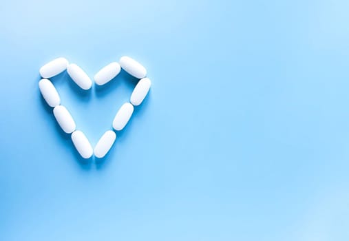 Pills of vitamin in the shape of heart on soft blue background.