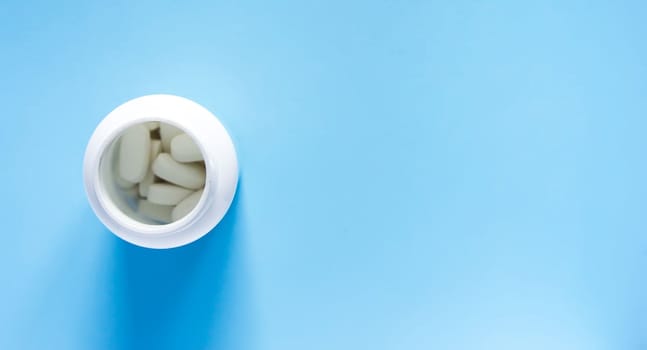 Pills of vitamin in the opened white plastic container on soft blue background.
